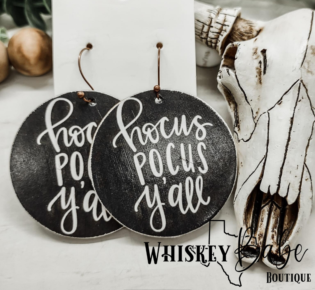 Wooden circle earrings with black background and Hocus Pocus Y’all written in white script.