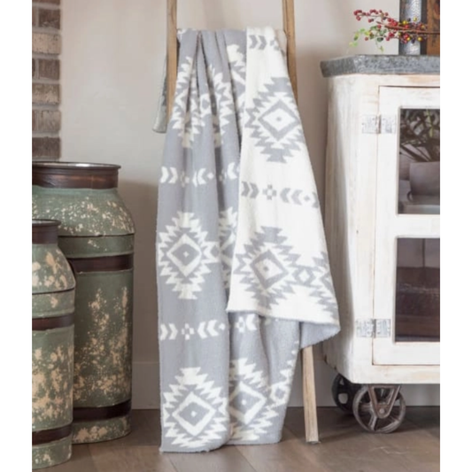 Gray and white patterned throw blanket draped over a wooden ladder in a room with decorative elements.