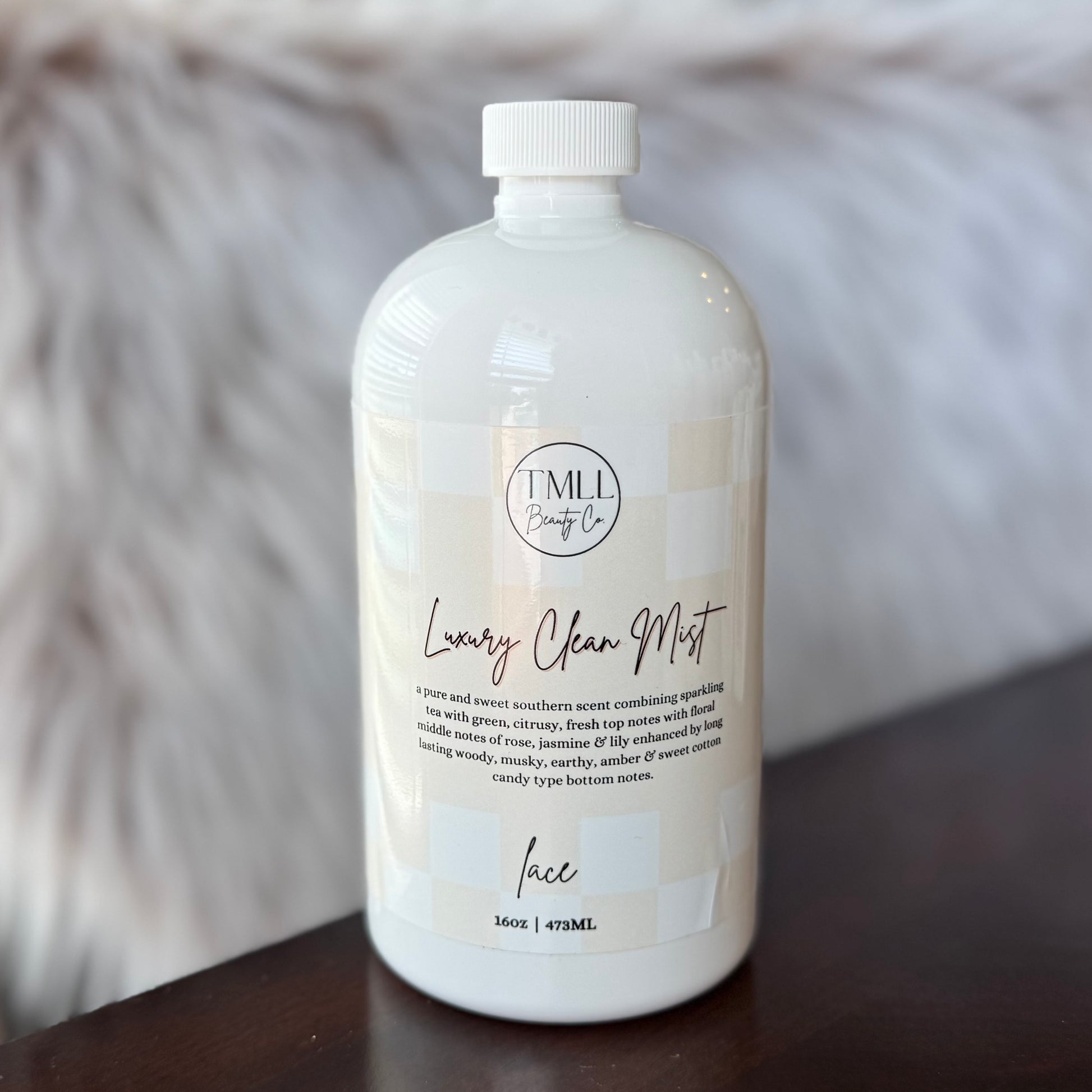 White bottle of Lace Luxury Clean Mist on a wooden surface with a blurred background