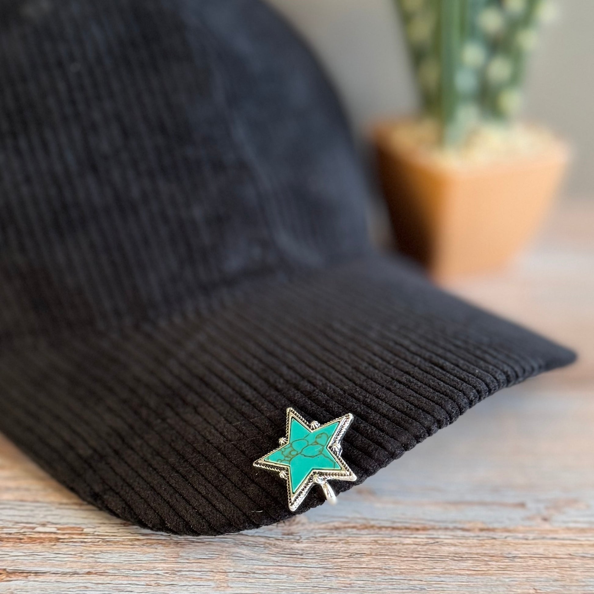 Black ribbed knit cap with a turquoise star-shaped pin on a wooden surface.