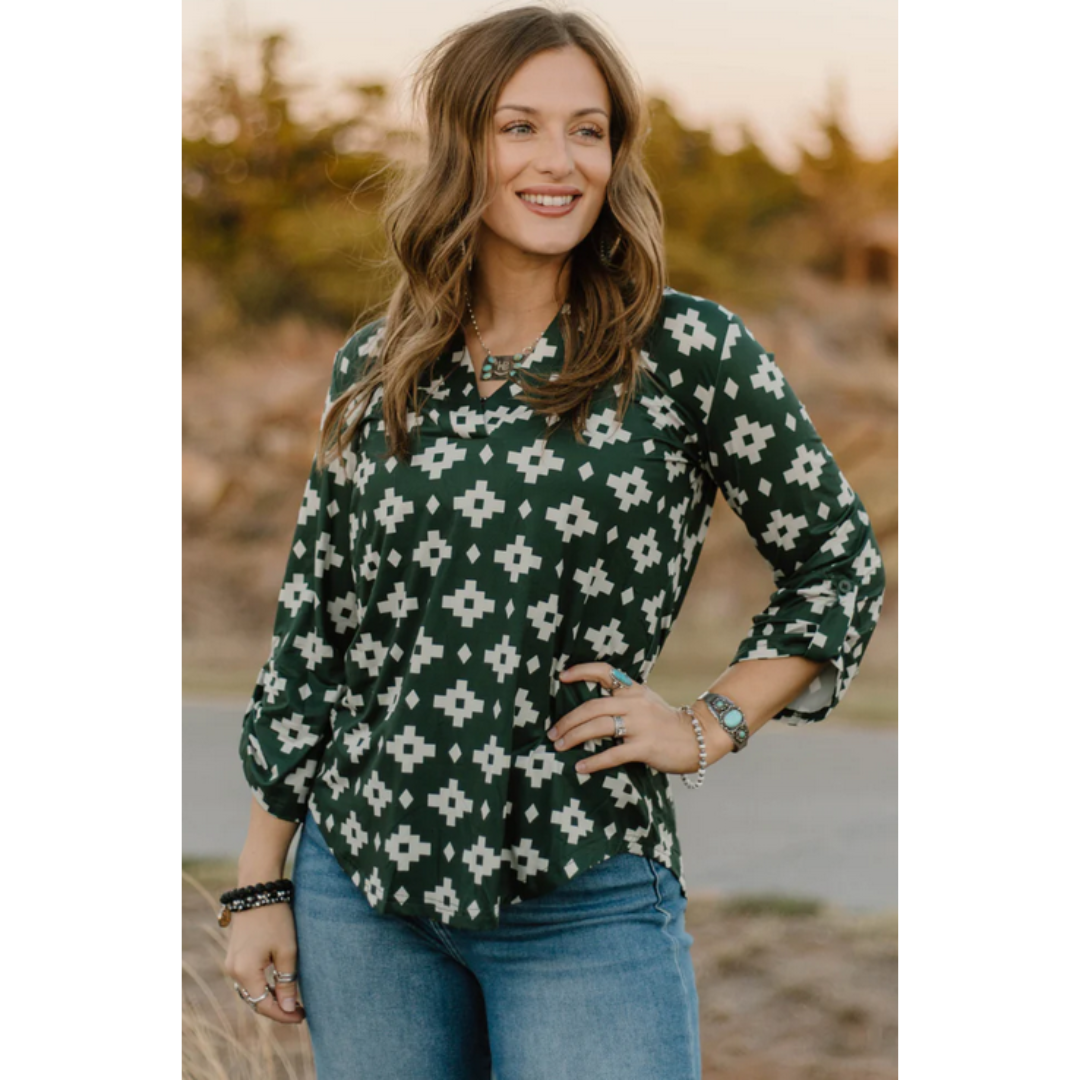 Woman wearing a green aztec patterned blouse standing outdoors with a blurred natural background
