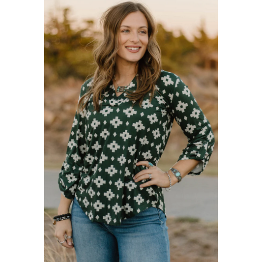 Woman wearing a green aztec patterned blouse standing outdoors with a blurred natural background