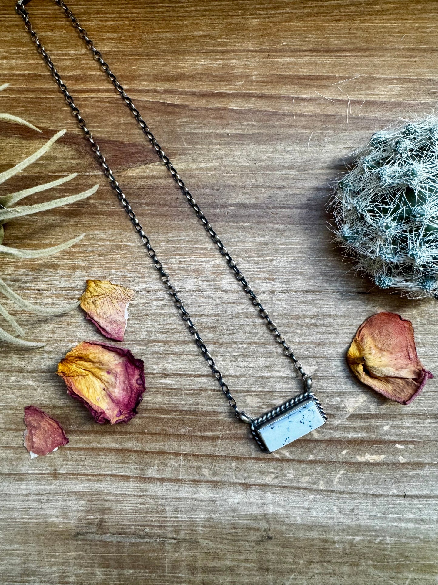 Necklace with a rectangular pendant on a wooden surface with dried flowers.