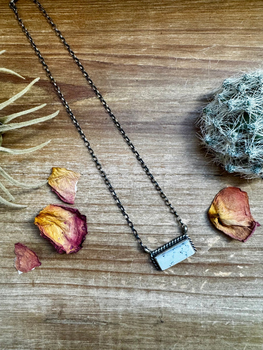 Necklace with a rectangular pendant on a wooden surface with dried flowers.