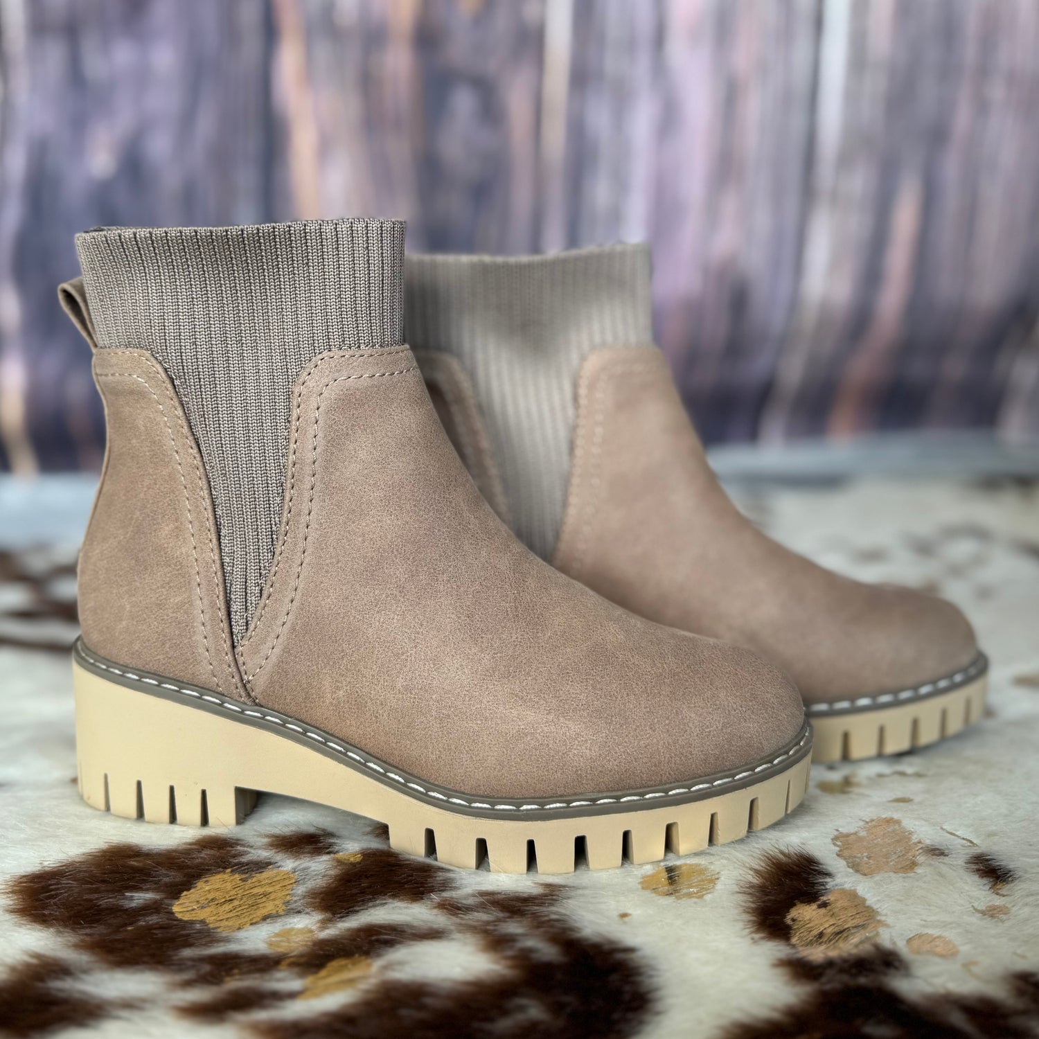 Pair of beige ankle boots with gray elastic cuffs on a patterned surface.