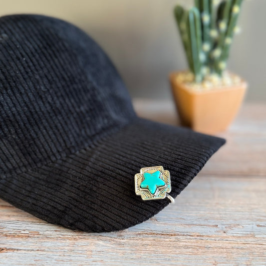 Black corduroy jacket with a turquoise and gold brooch on a wooden surface, cactus in the background.