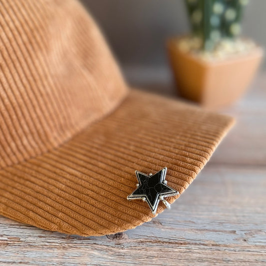 Brown corduroy hat with a black star pin on a wooden surface, blurred plant in the background