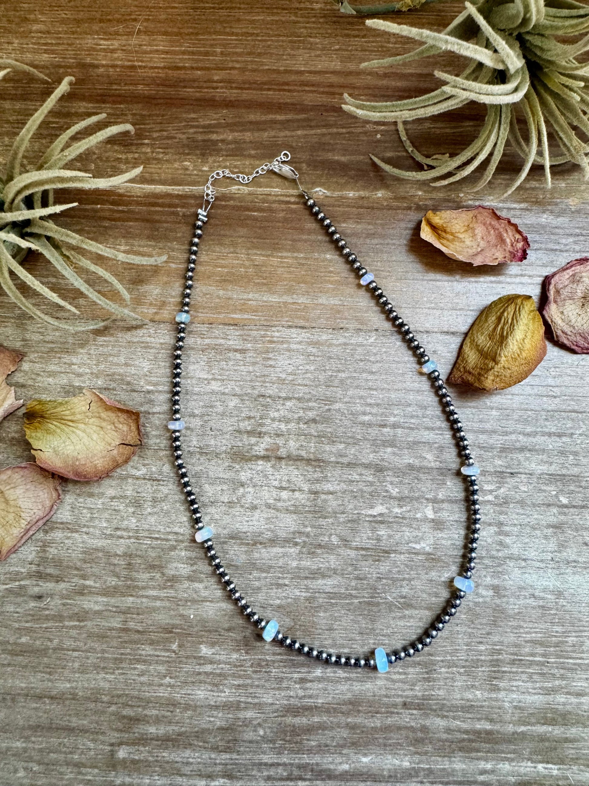 Necklace with black and blue beads on a wooden surface with dried leaves and plants.