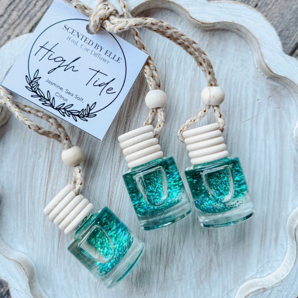 Three teal glittery diffusers with wooden beads on a white textured surface, featuring high tide scent.