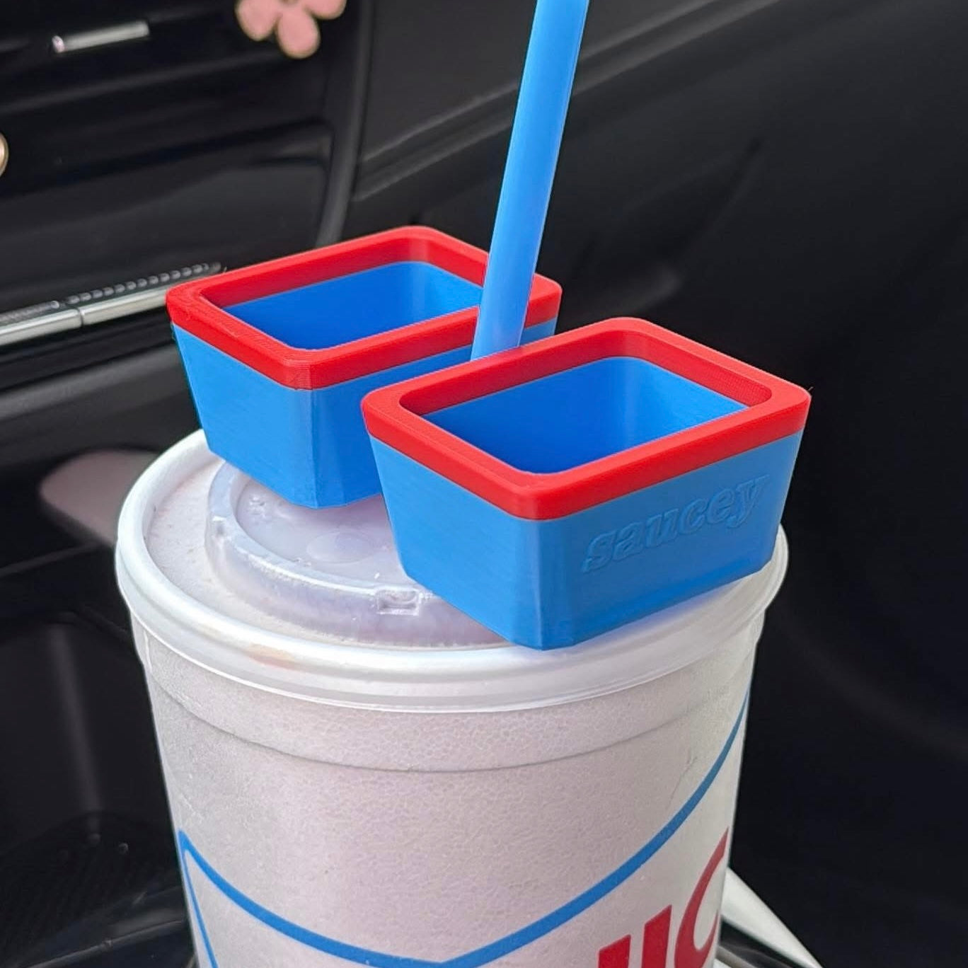 Two blue dipping sauce holders with red rims on a cup inside a car.