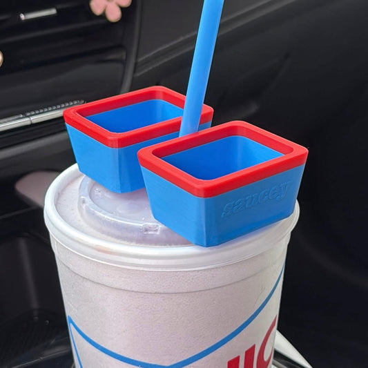 Two blue dipping sauce holders with red rims on a cup inside a car.