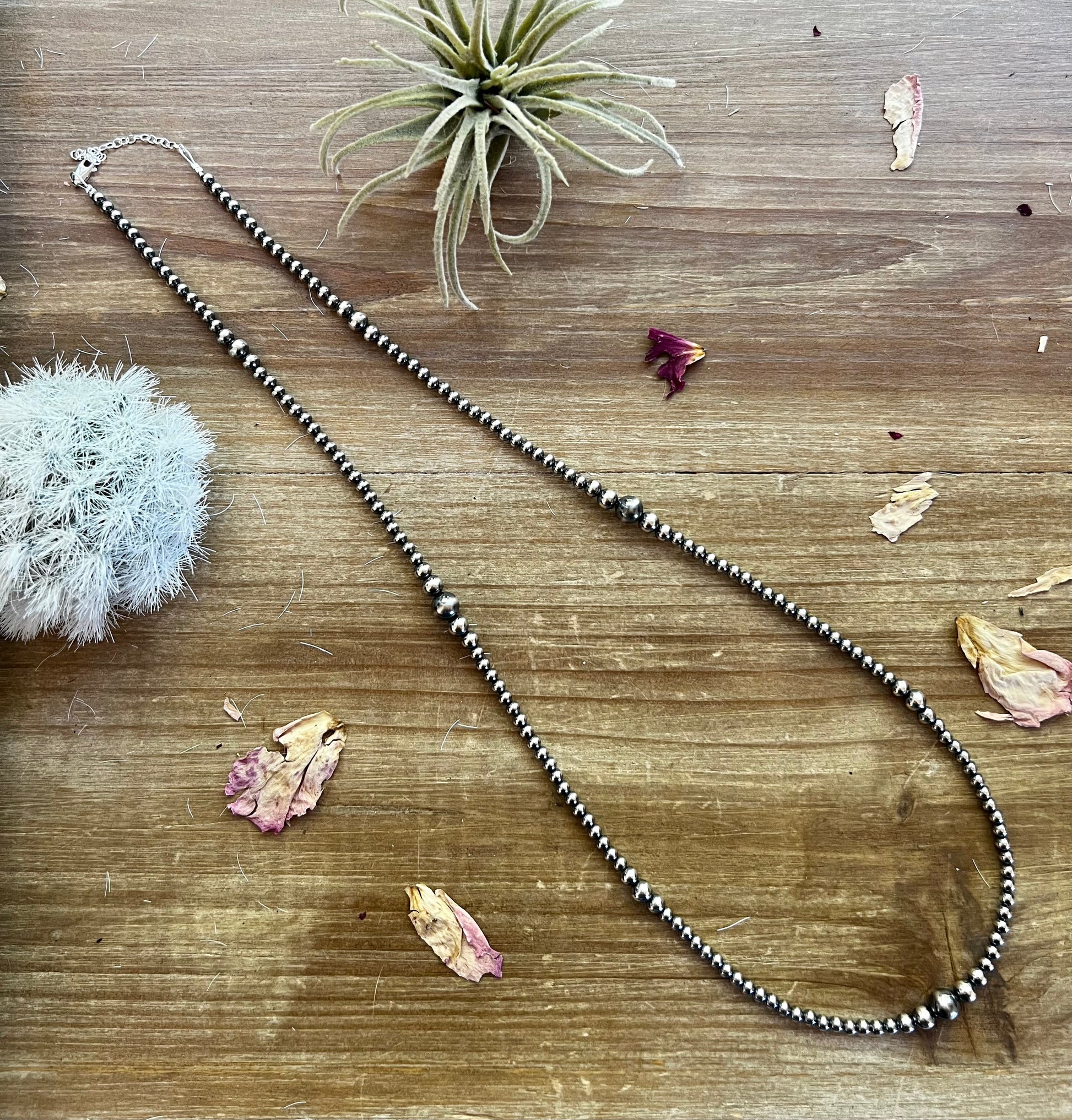 Beaded necklace on a wooden surface with dried flowers and an air plant.