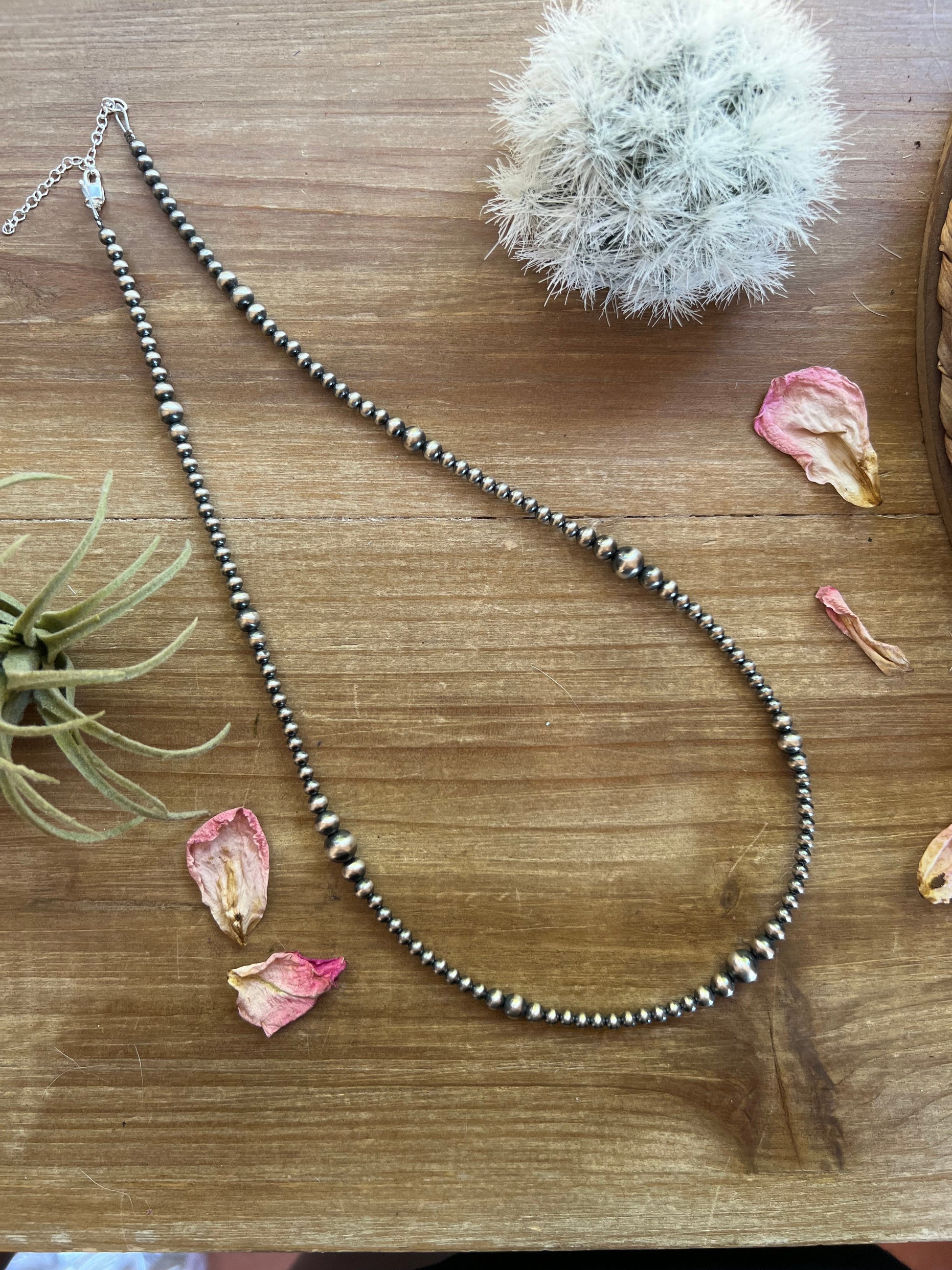 Necklace with beaded chain on a wooden surface with dried flowers and plants.